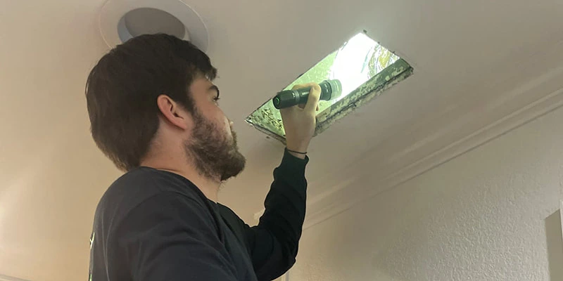 Technician inspecting ceiling air duct with flashlight
